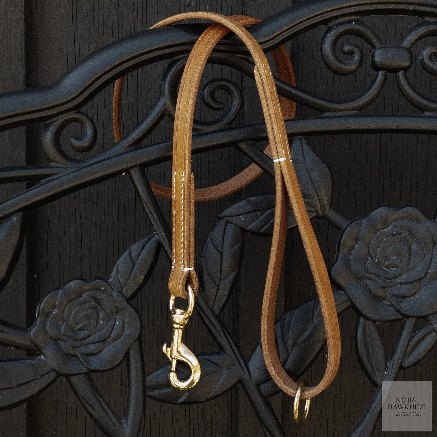 Classic handmade leather dog leash hanging on decorative wrought iron gate.
