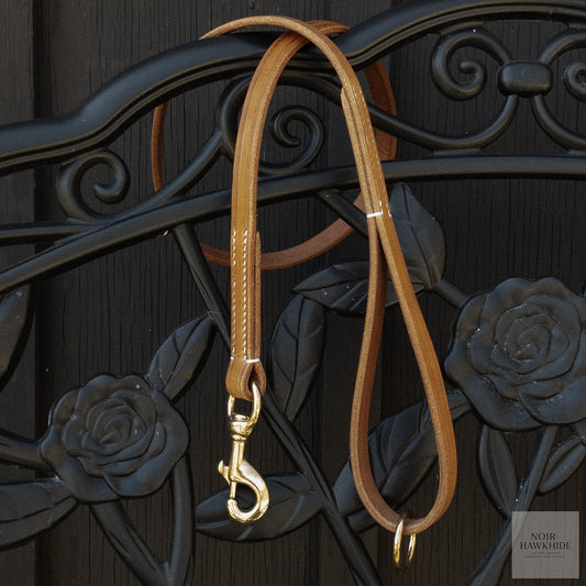 Classic handmade leather dog leash hanging on decorative wrought iron gate.