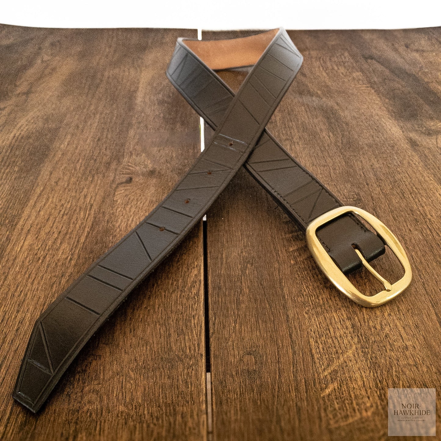 Handcrafted black leather belt with geometric hand-tooled pattern photographed on a wooden table.