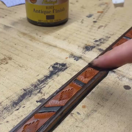 Hand applying antique finish to a hand-tooled Western geometric leather dog leash during the handmade leathercraft process