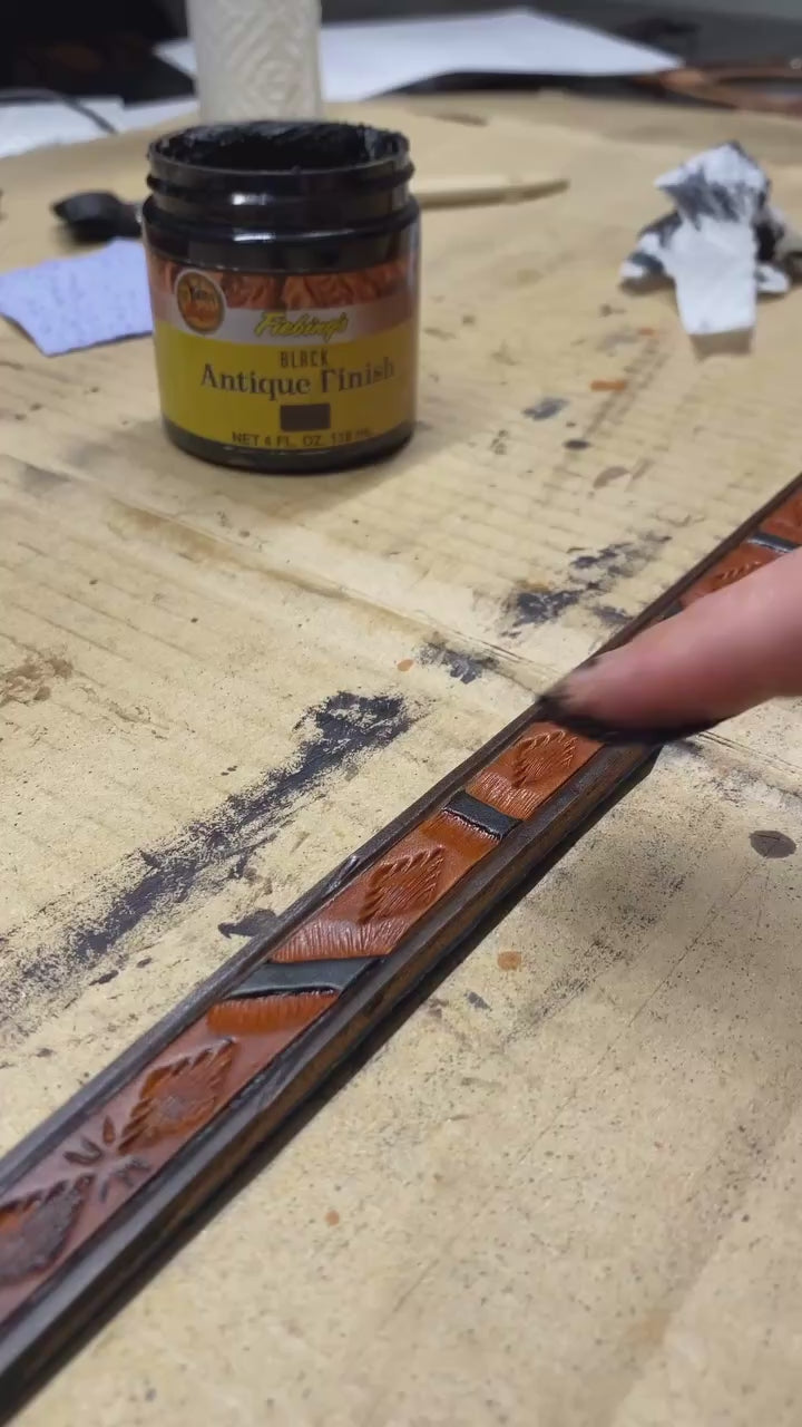Hand applying antique finish to a hand-tooled Western geometric leather dog leash during the handmade leathercraft process